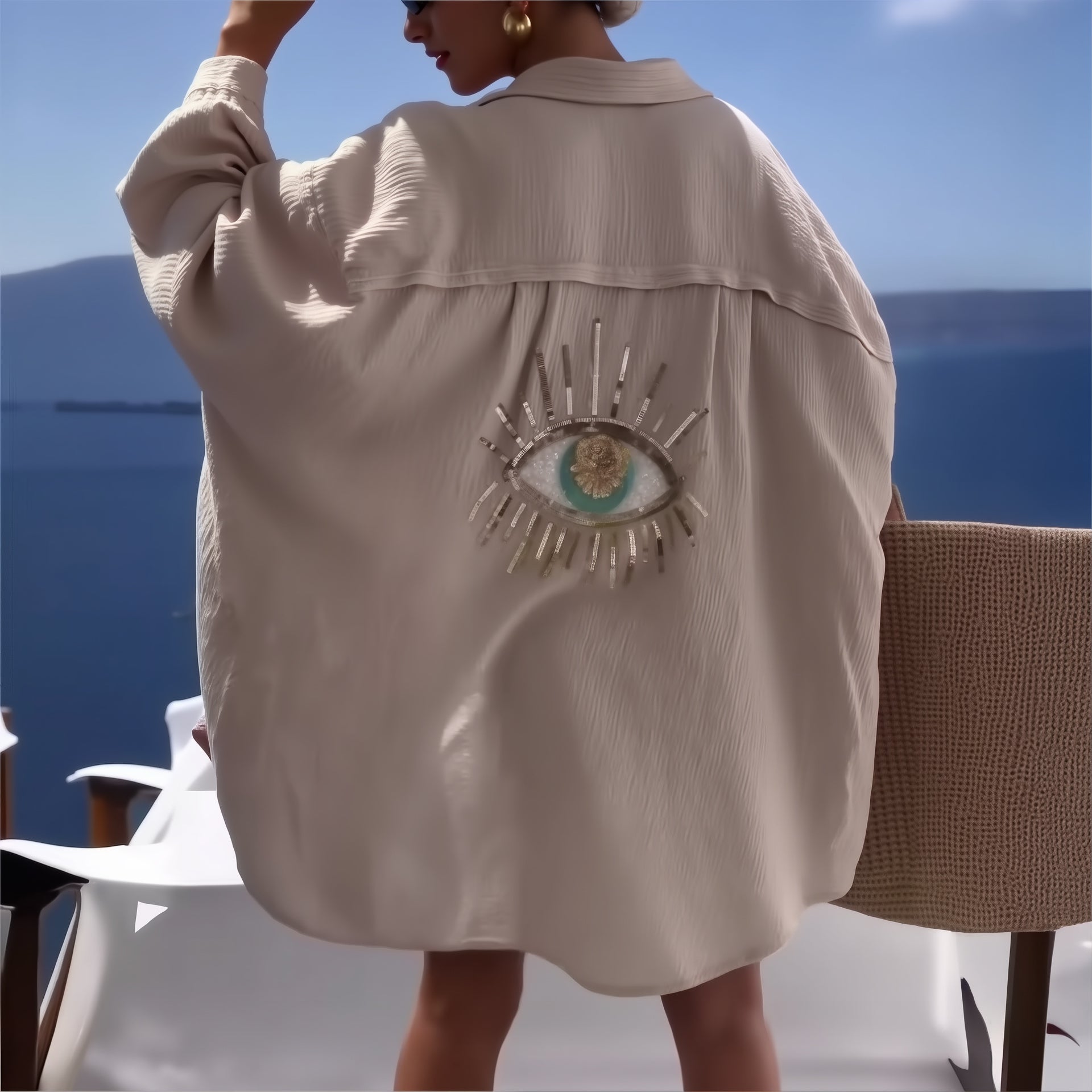 Cream linen shirt with eye embroidery detail, worn over bikini at seaside, perfect for beach cover-up styling.