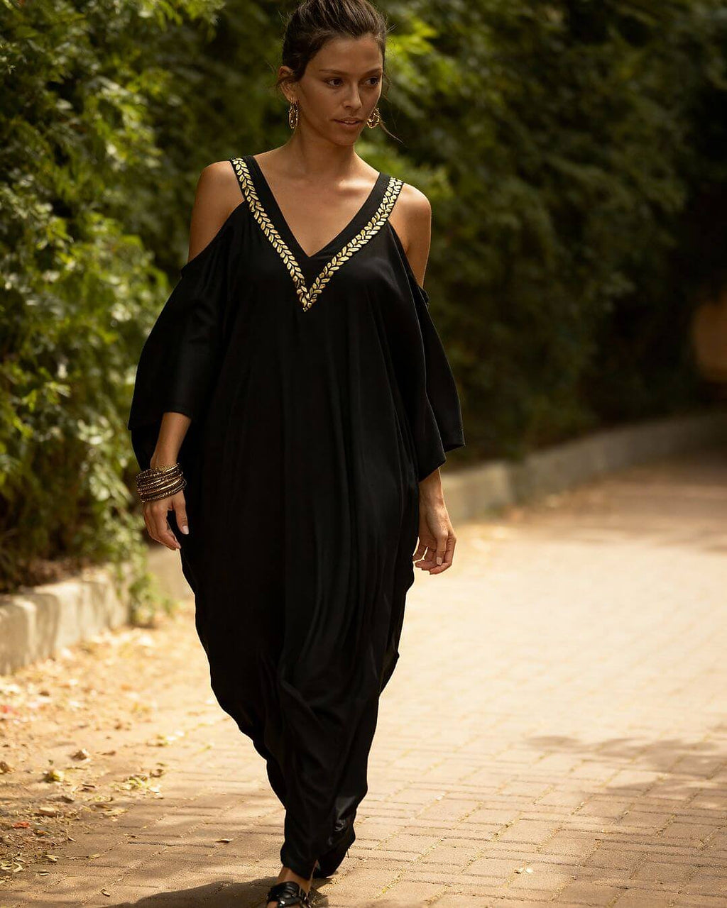 Woman wearing black cold-shoulder bikini cover-up with gold embroidered neckline detail, styled with gold bracelets.