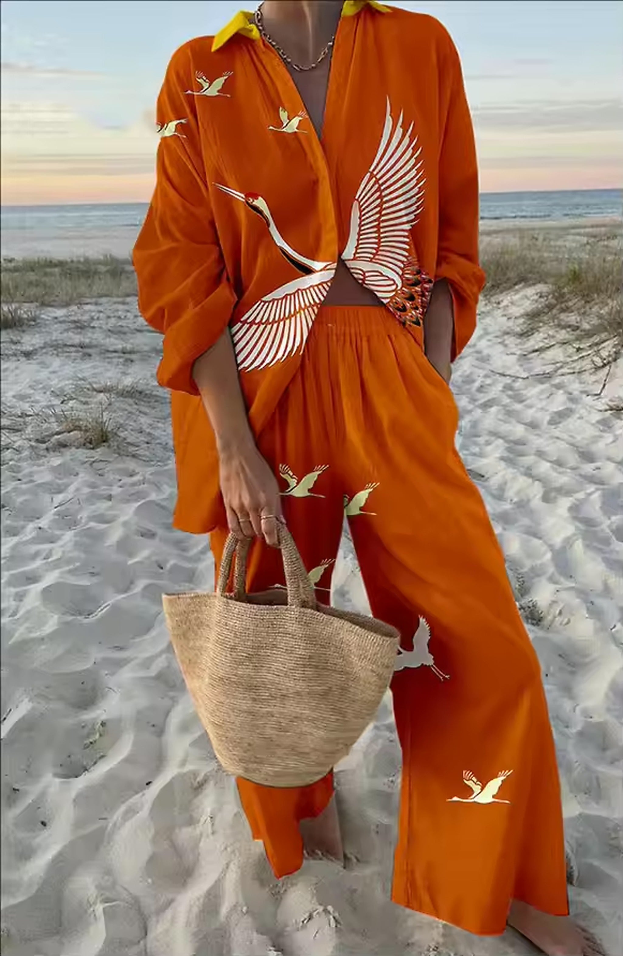 Woman wearing orange Savanna Siren bikini with bird print shirt on sandy beach at sunset