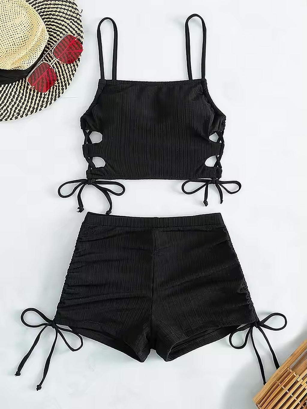 Black ribbed bikini with side-tie cutouts and adjustable straps, styled with straw hat and beach accessories
