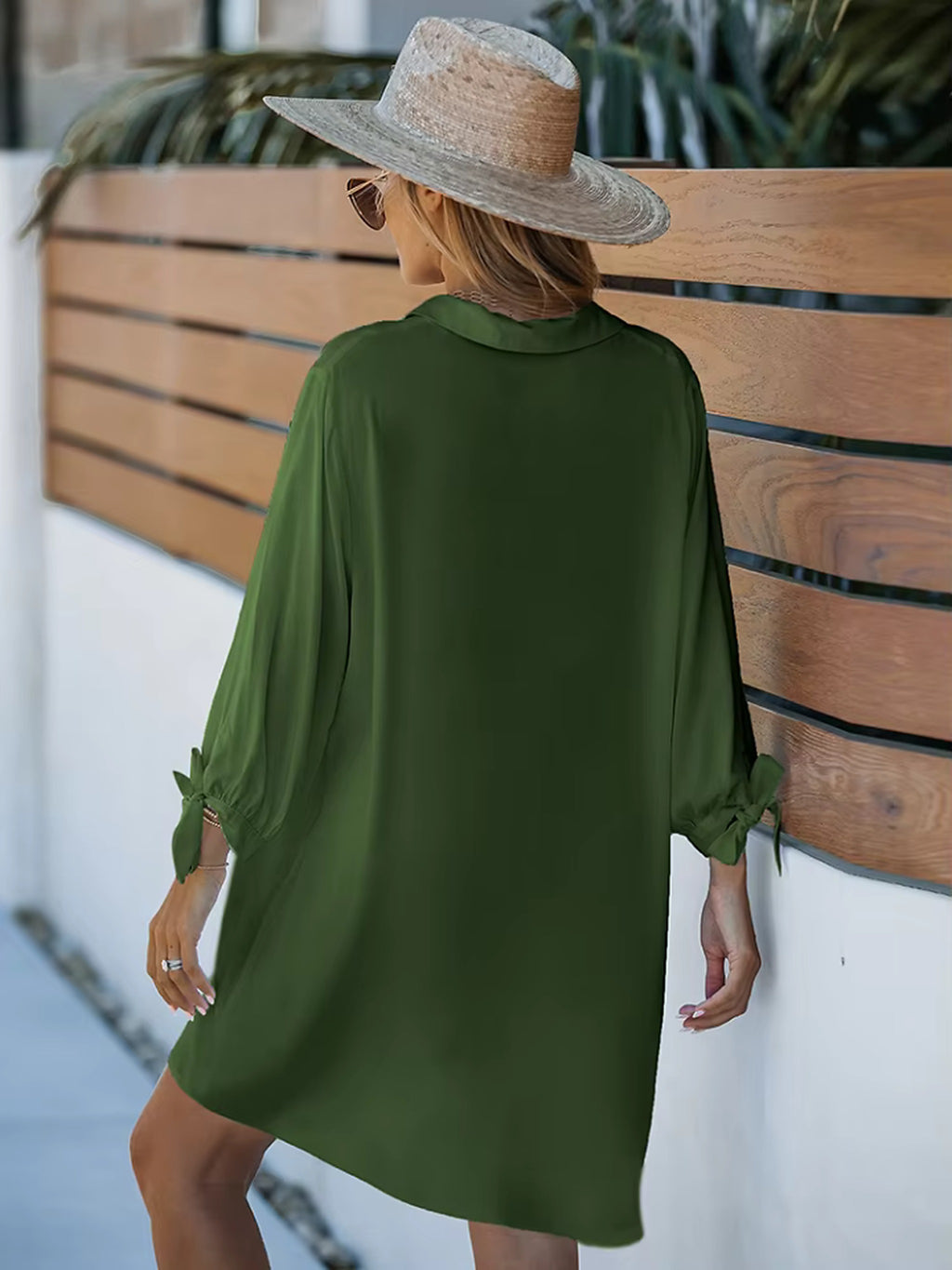 Woman wearing olive green button-up swim shirt cover-up over bikini, styled with straw hat and sunglasses