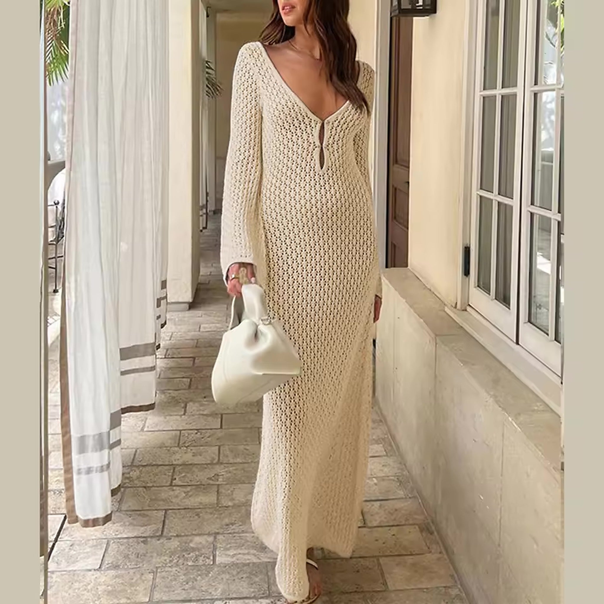 Woman wearing cream knit Marbella Muse bikini cover-up with V-neckline and long sleeves in coastal hallway setting.