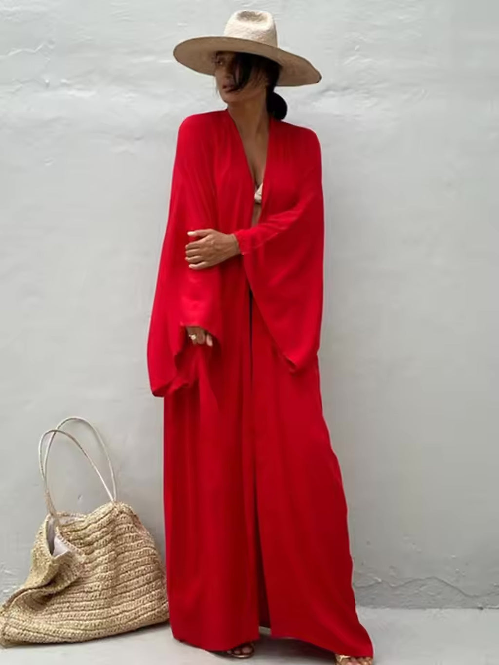 Woman wearing red Luna Mare cover-up with straw hat and woven beach bag by white wall