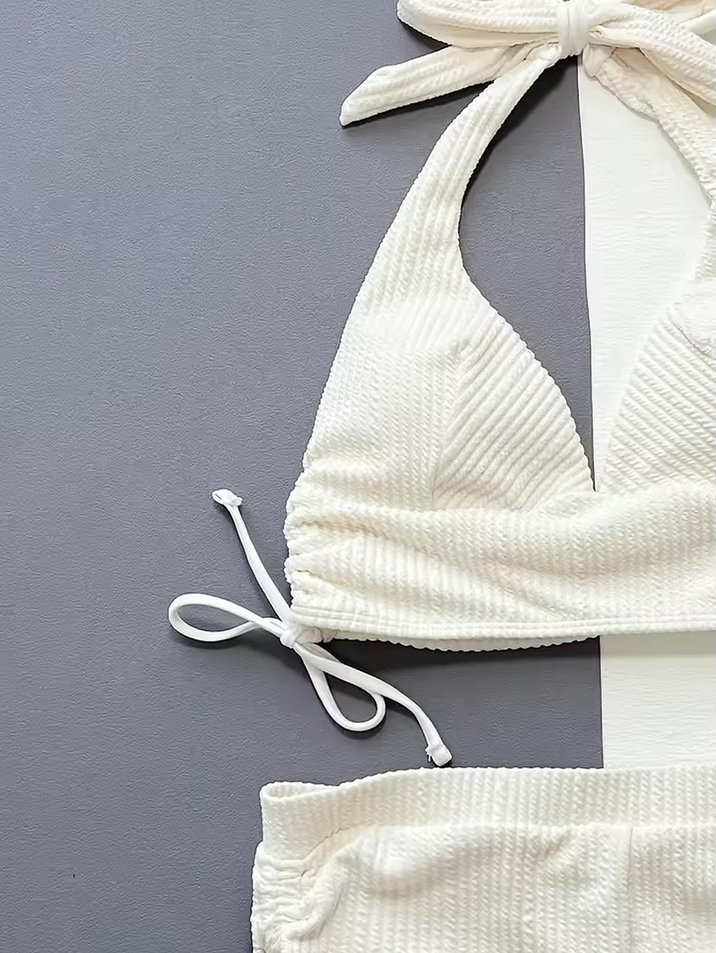 White textured bikini top with halter neck ties and adjustable side straps on gray background