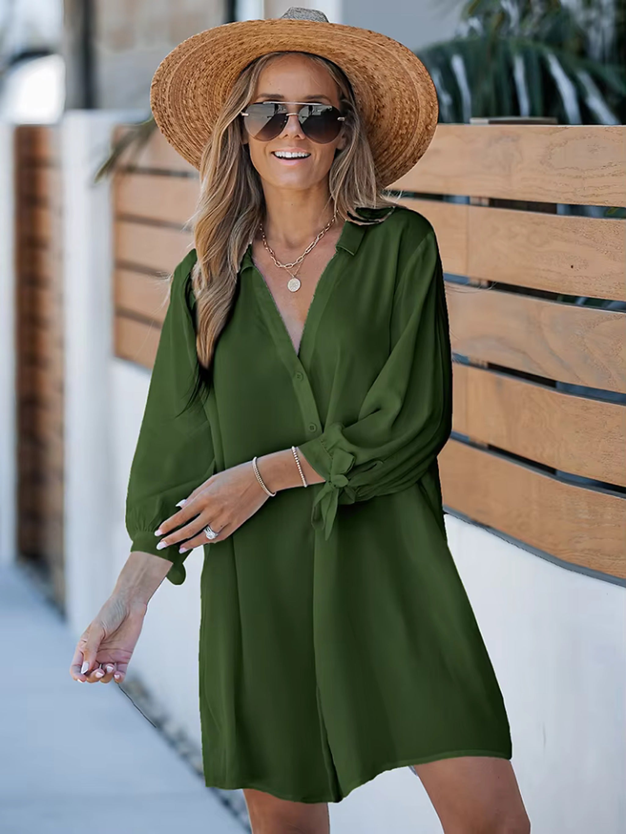 Woman wearing olive green wrap cover-up dress with straw hat and sunglasses by wooden bench