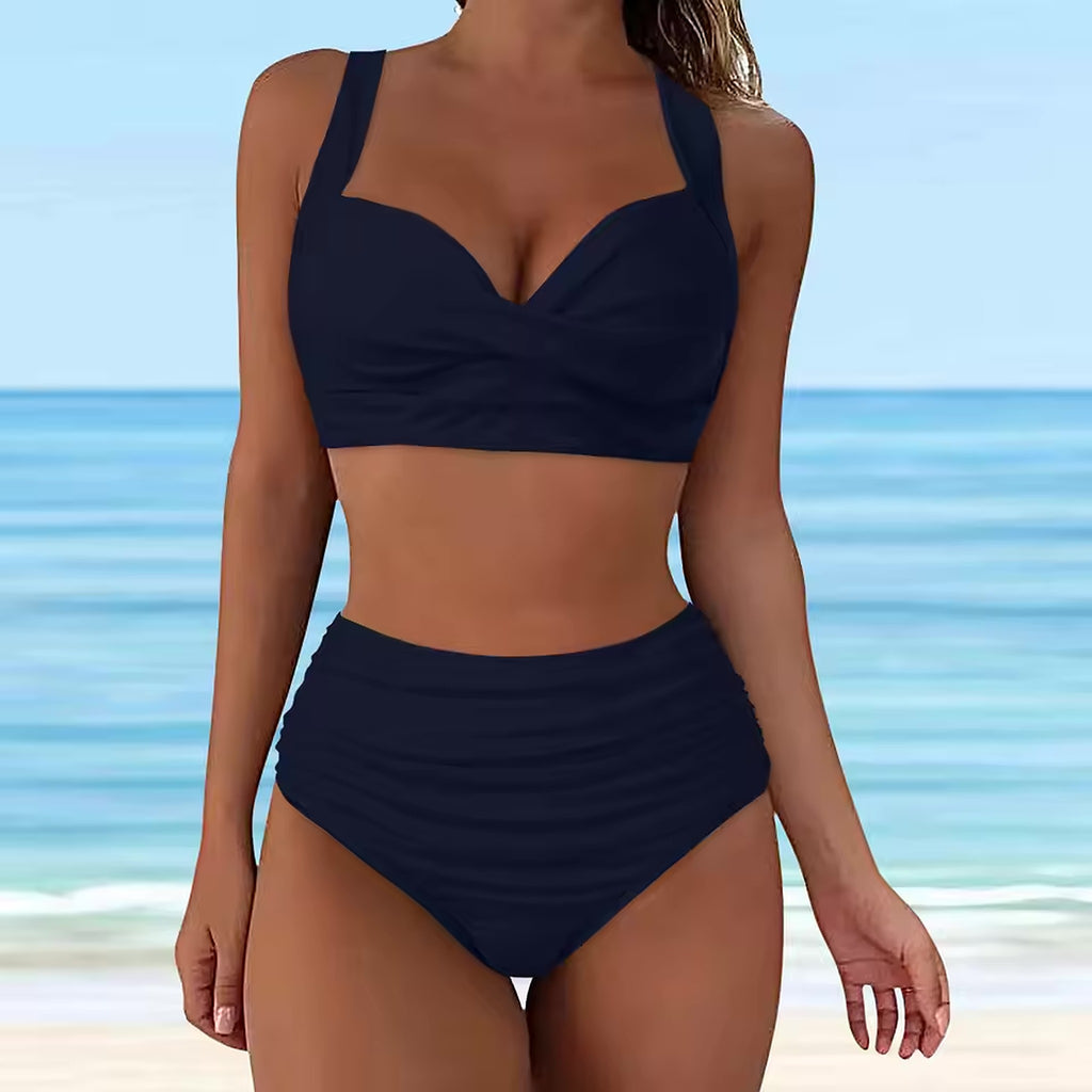 Woman wearing navy blue sweetheart neckline bikini top with high-waisted bottom on beach with ocean backdrop