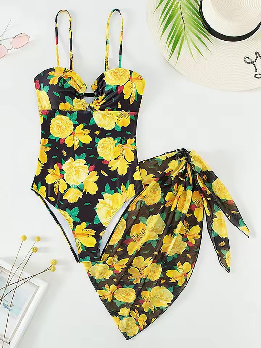 Yellow floral bikini with matching sarong on black background, styled with straw hat and sunglasses.