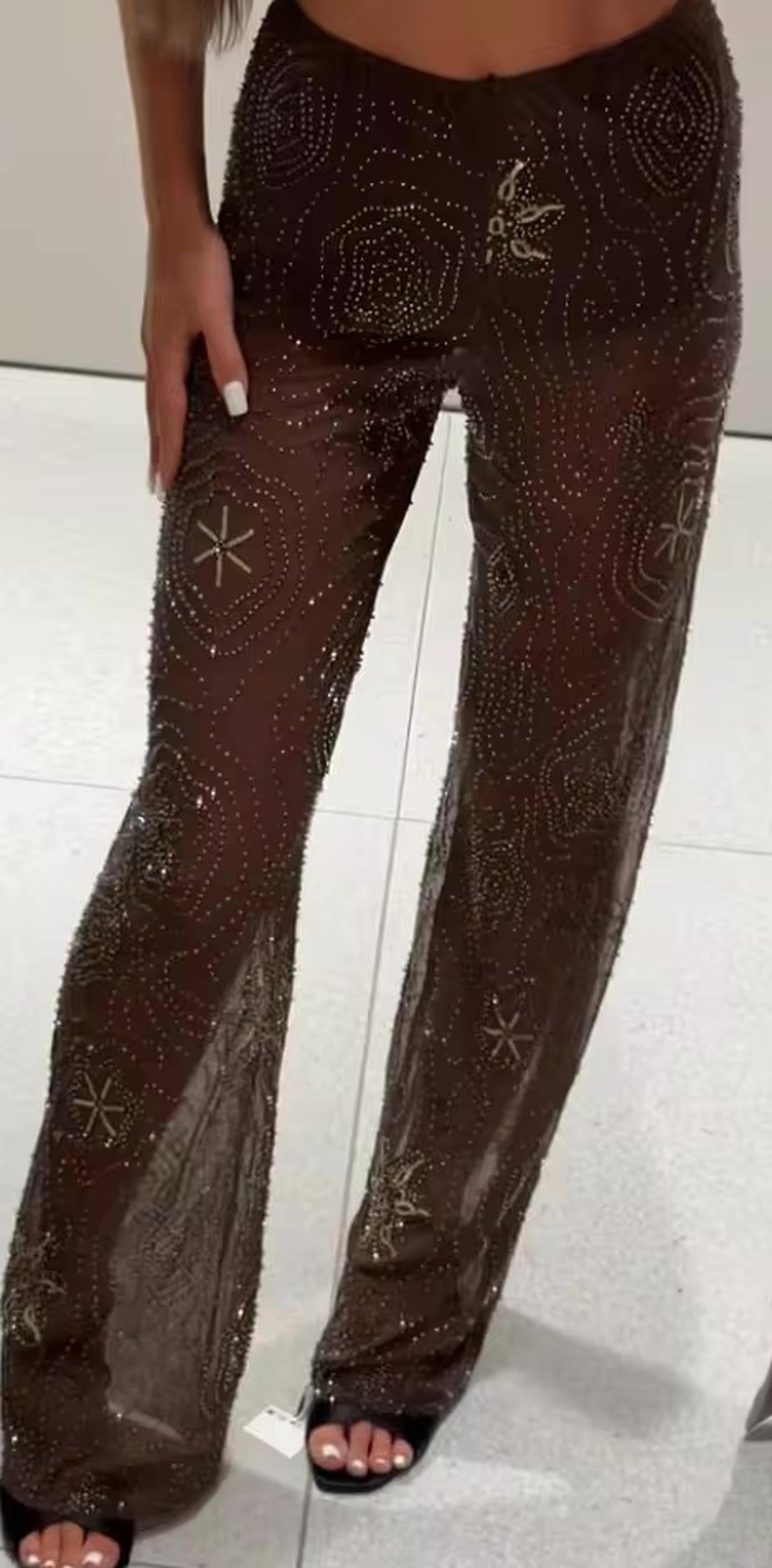 Brown beaded mesh pants with geometric patterns and snowflake embellishments, featuring a white side stripe and wide leg cut.