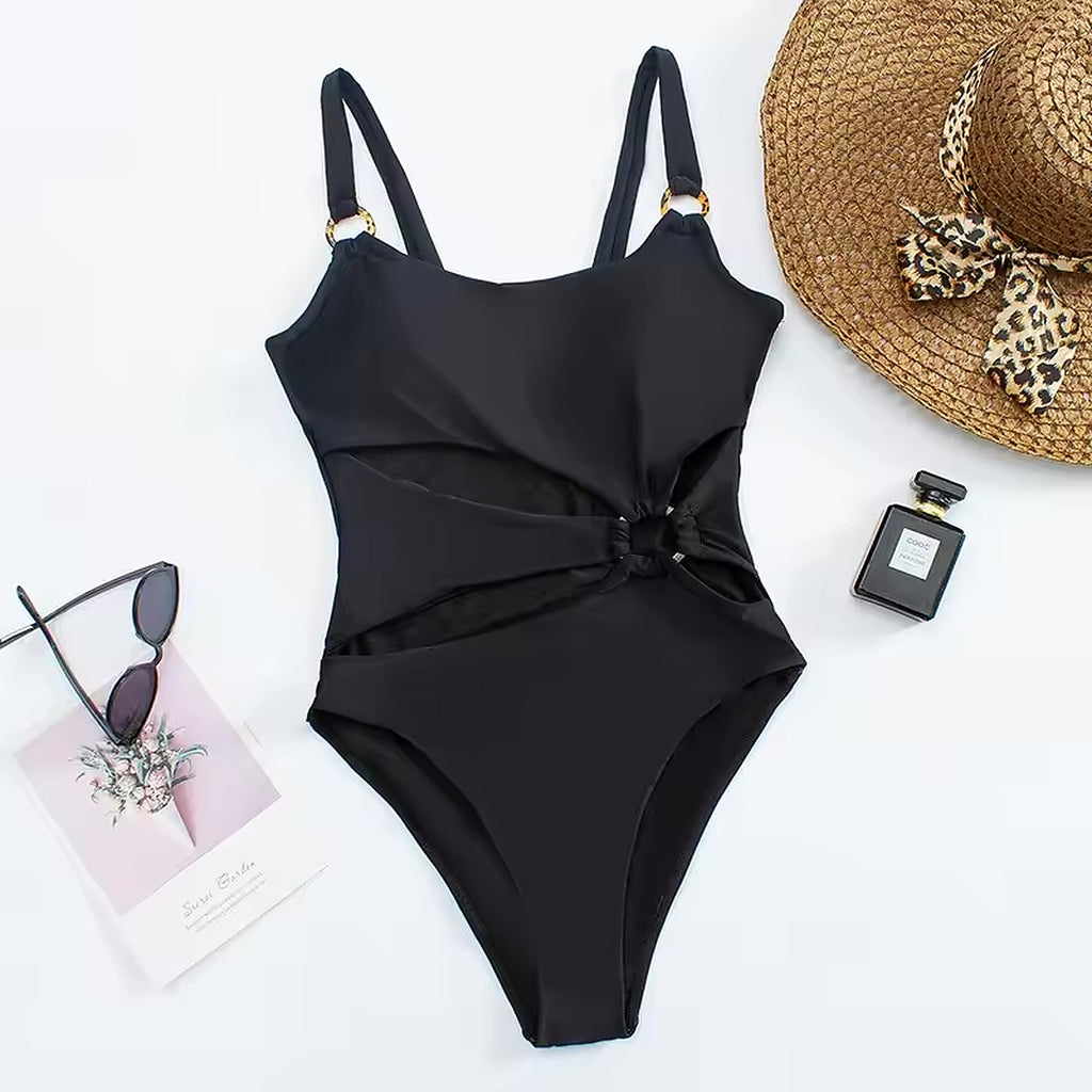 Black wrap-front one-piece swimsuit with gold hardware and adjustable straps, styled with straw hat and sunglasses