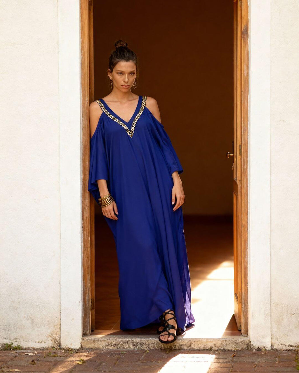 Woman wearing navy blue cold-shoulder bikini cover-up with gold chain neckline detail, standing in doorway.