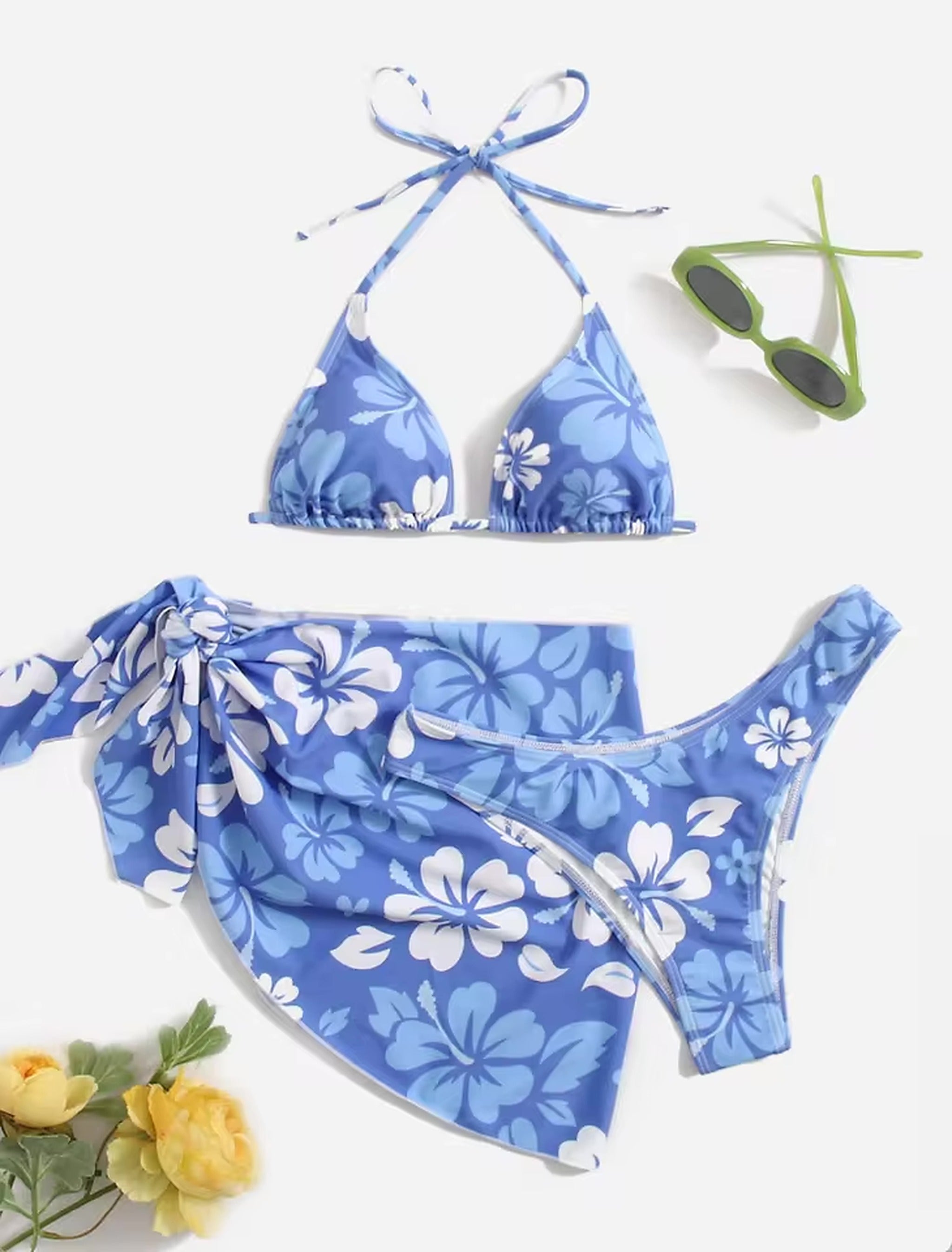 Blue floral bikini set with halter top and matching sarong wrap, styled with sunglasses and yellow flowers.
